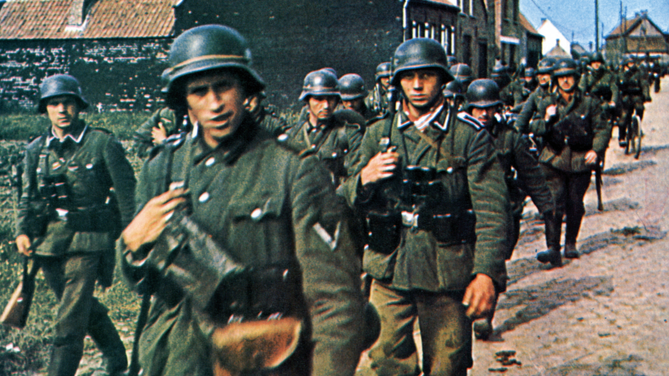 Wehrmacht infantrymen march through a Belgian town to occupy territory overrun by armored divisions.