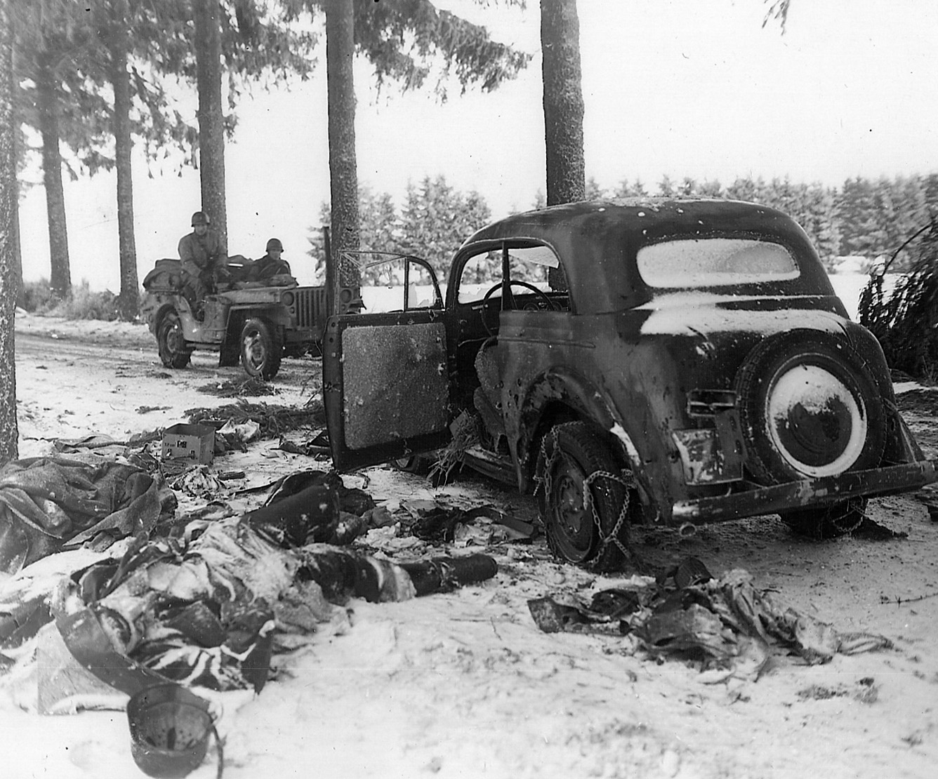 A Nazi SS captain lies dead behind his command car as U.S. soldiers survey the scene near Houffalize. 