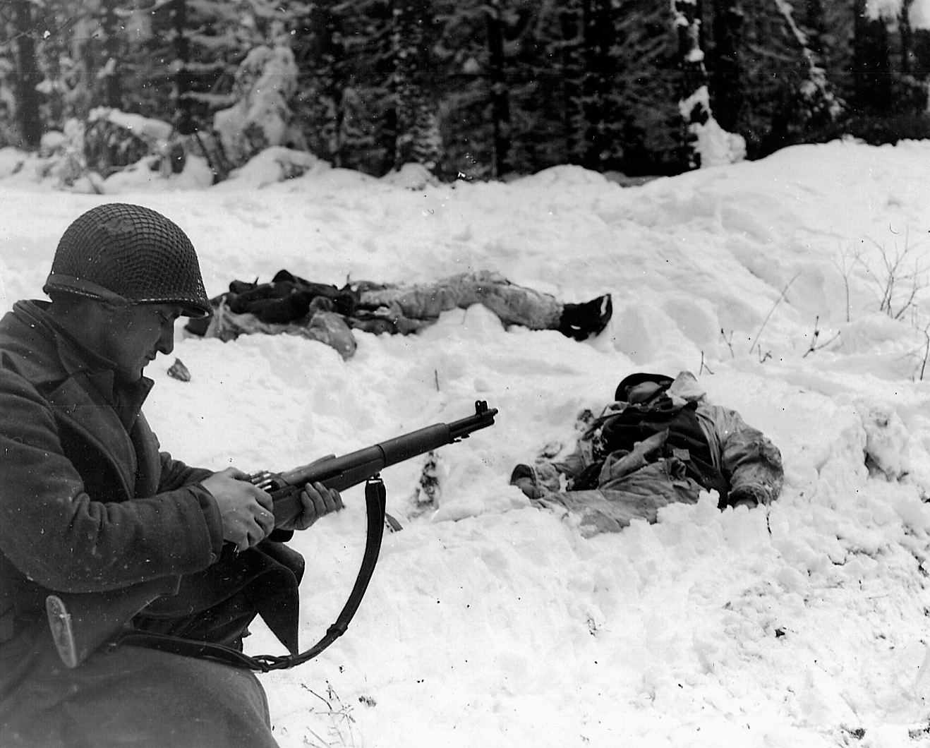 A soldier reloads his M-1 rifle near the bodies of two dead Germans in the bitter cold of January, 1945. 
