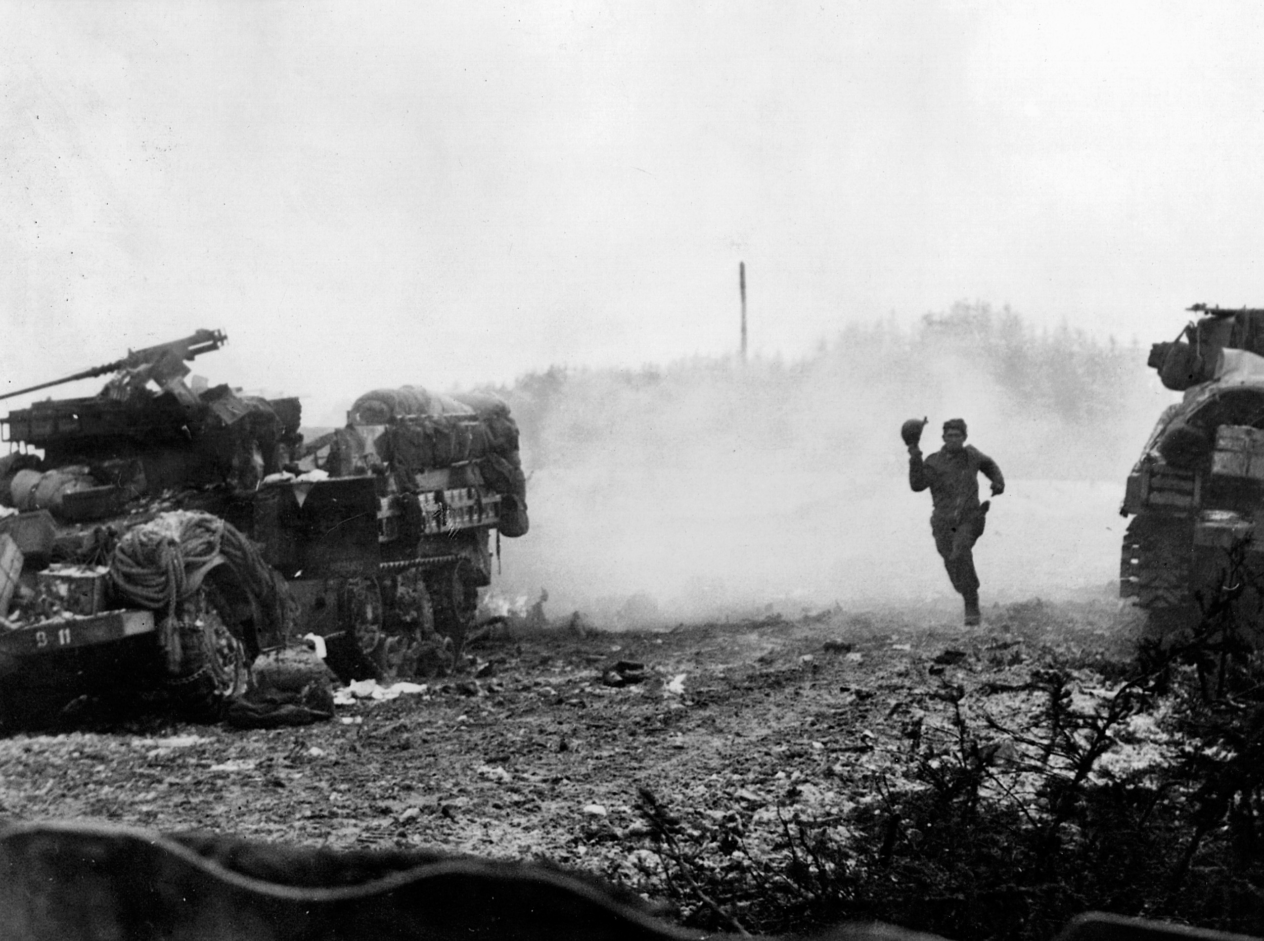 A U.S. soldier runs past a halftrack still smoking from a direct hit in Langlois, Belgium outside Houffalize.