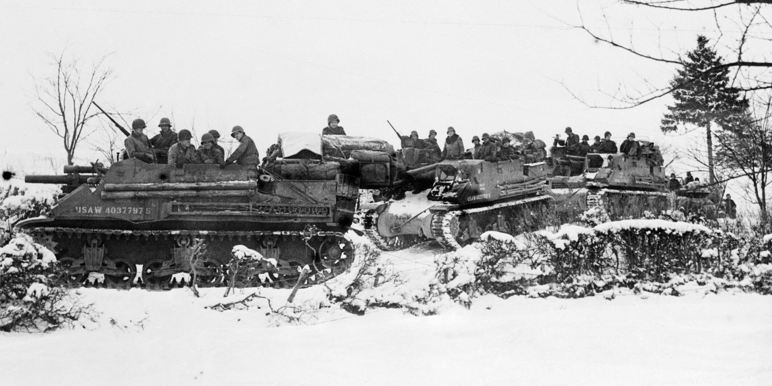 American tanks and armored gun carriers drive over snow-covered terrain to Samree during the Battle of the Bulge. Capture of the city opened the way to Houffallize, heart of the Bulge.