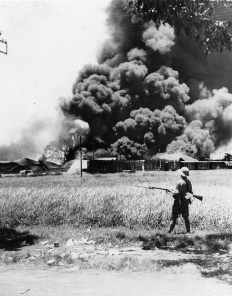 During the early months of 1942, the Allied forces in the Pacific suffered numerous setbacks at the hands of marauding Japanese. Here, a Japanese soldier watches several oil storage tanks go up in flames.