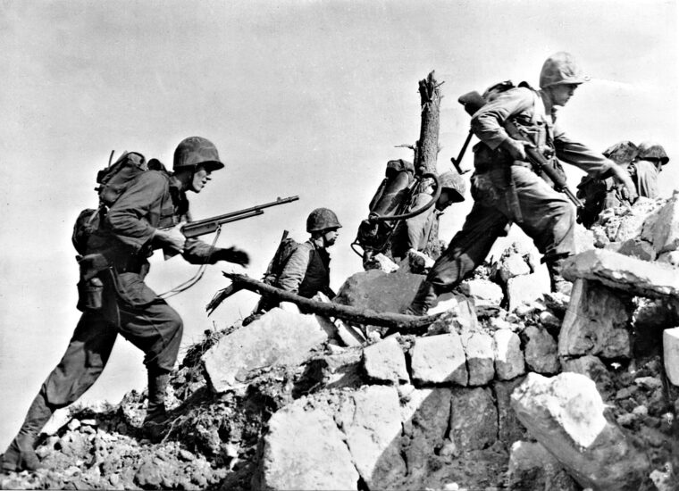 U.S. Marines make their way across a low stone wall as they seek out hidden Japanese positions on bloody Okinawa.
