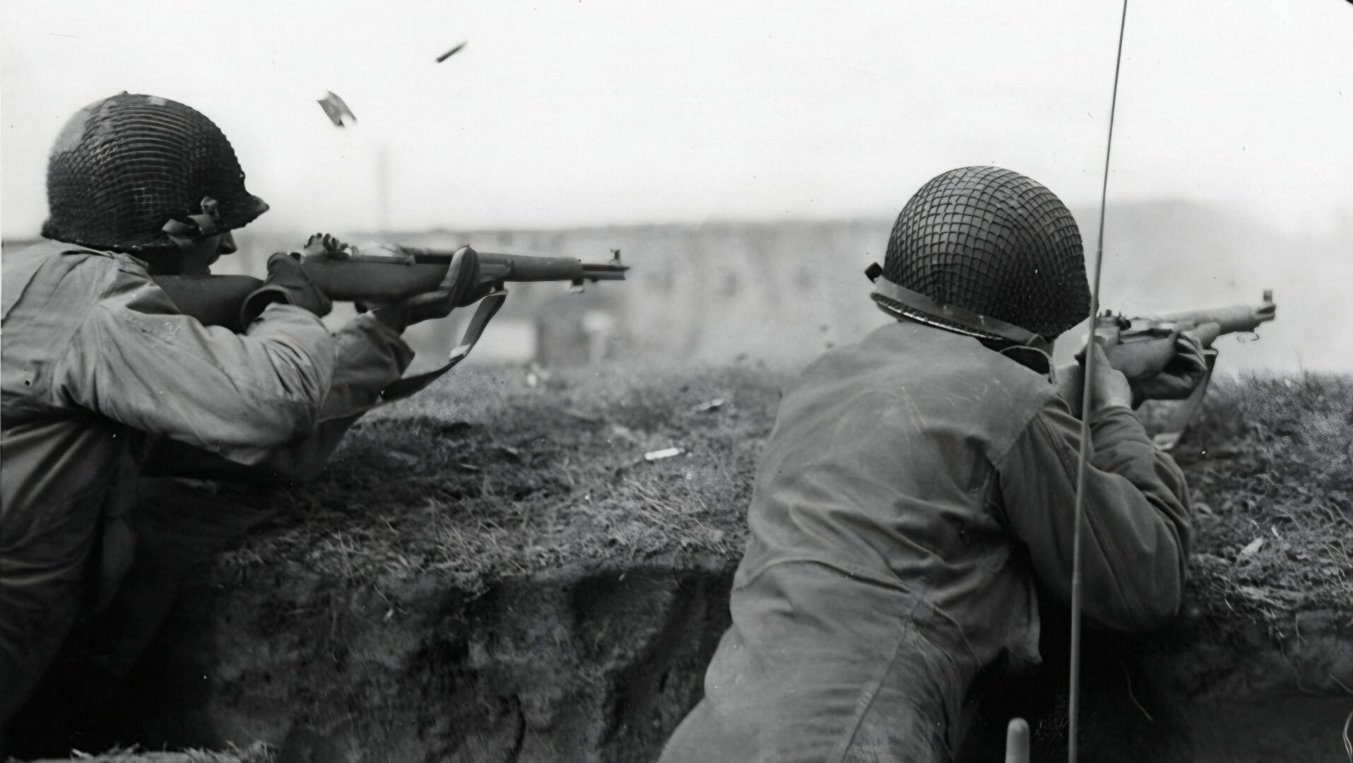Taking advantage of the minimal cover afforded by their foxhole, a pair of American soldiers provides suppressing fire in an effort to dislodge a German sniper
