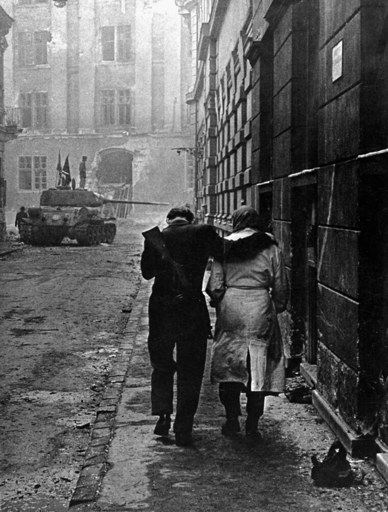 Wounded in the early street fighting, a Hungarian patriot is escorted to an aid station. Rebel headquarters at right is being guarded by a captured Russian tank, now sporting the independent national banner.