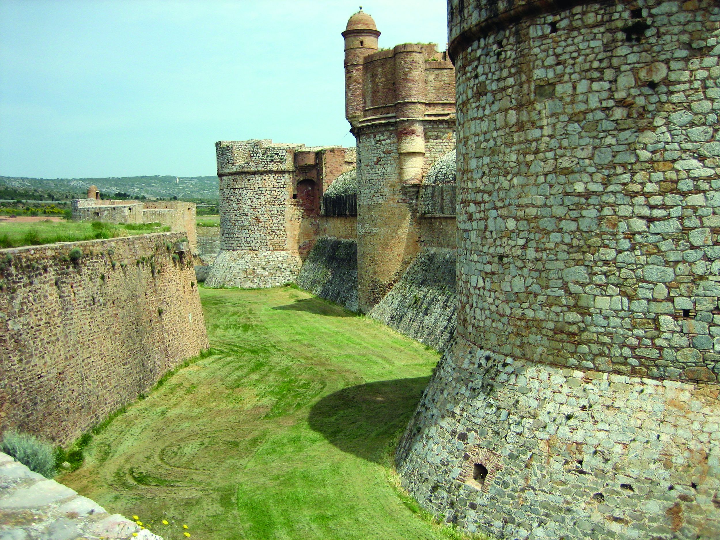 Salses is protected by a wide dry moat, glacis, and three independent pointed towers.