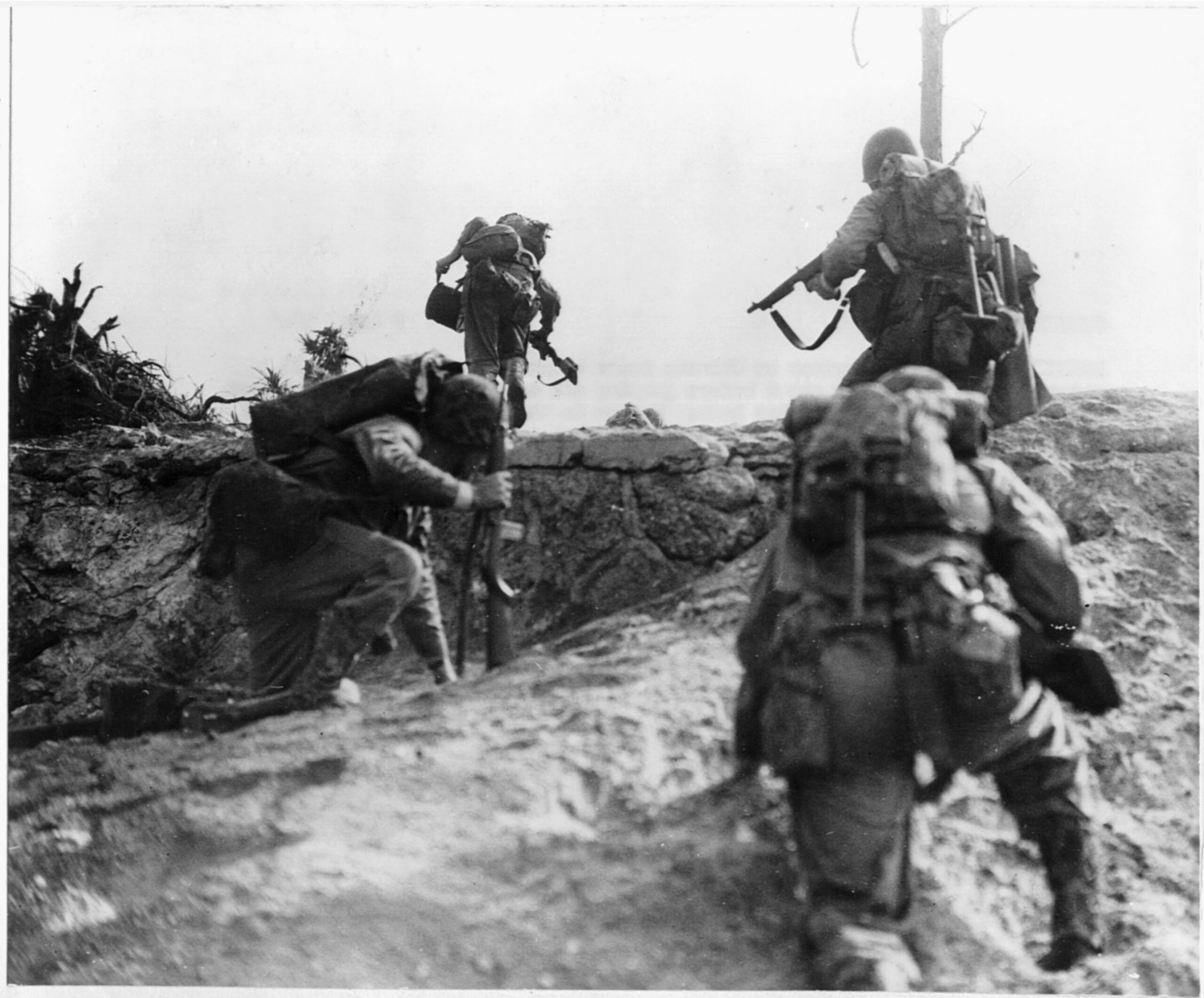 Marines advancing on the run. Two are carrying communications wire and radio equipment to stay in contact with other units.