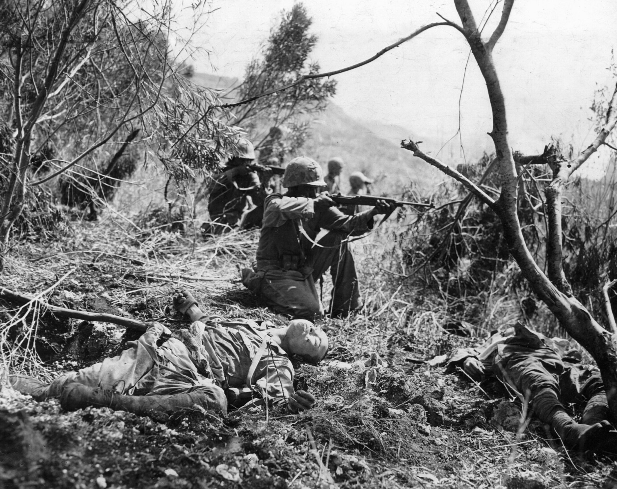 Surrounded by the bodies of slain Japanese soldiers, U.S. Marines open fire on an enemy position during their advance toward the western beach of the island.