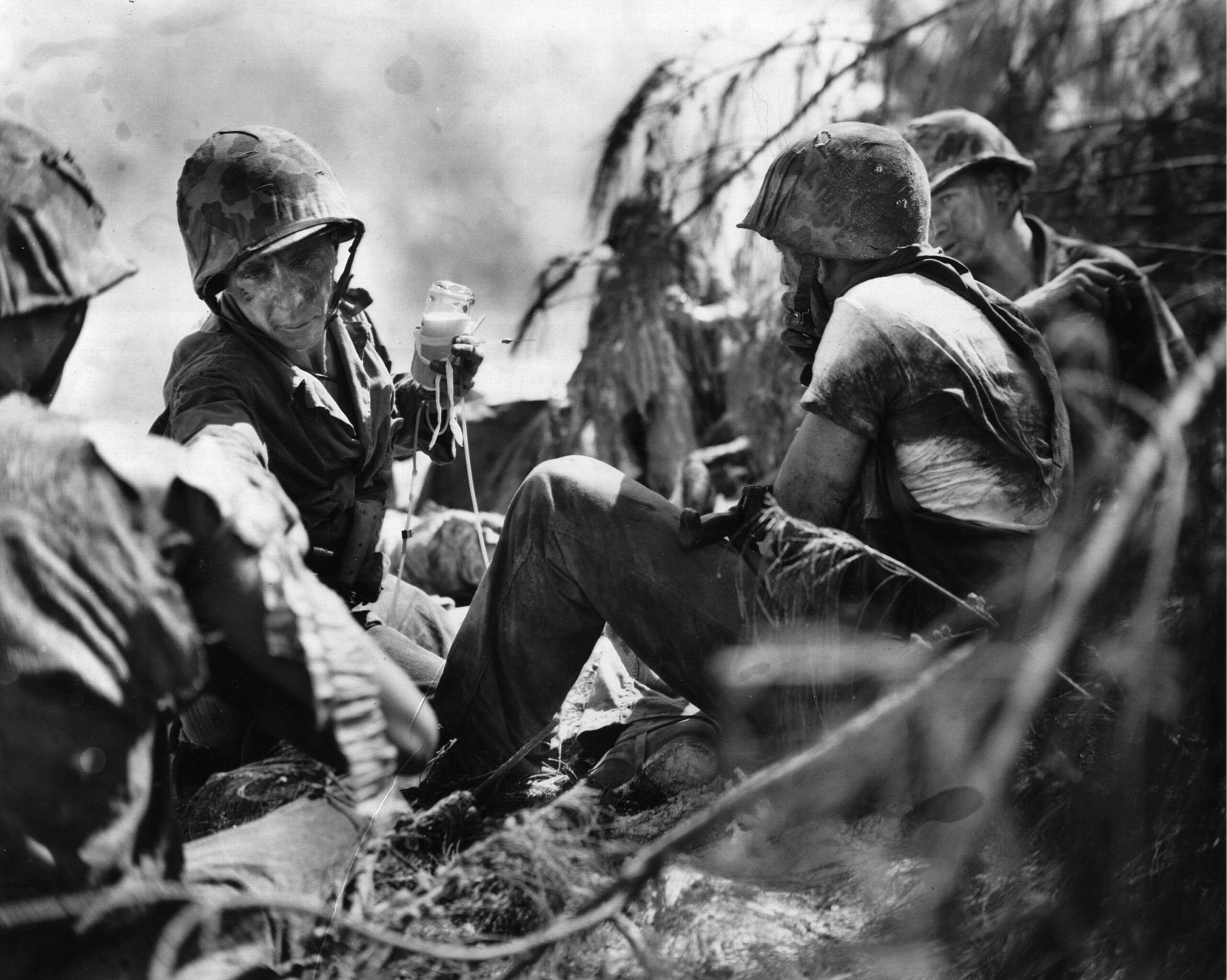 A hard-pressed Navy corpsman administers life-saving plasma to a group of wounded Marines on the beach.