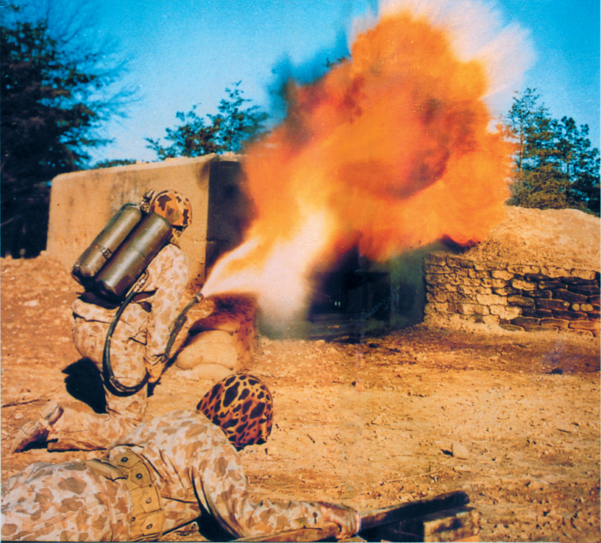 The M1 Flamethrower is seen here in use. The man at the bottom of the photo carried a dummy pole charge ready to thrust it into the pillbox opening once the flame has driven the occupants to cover. 