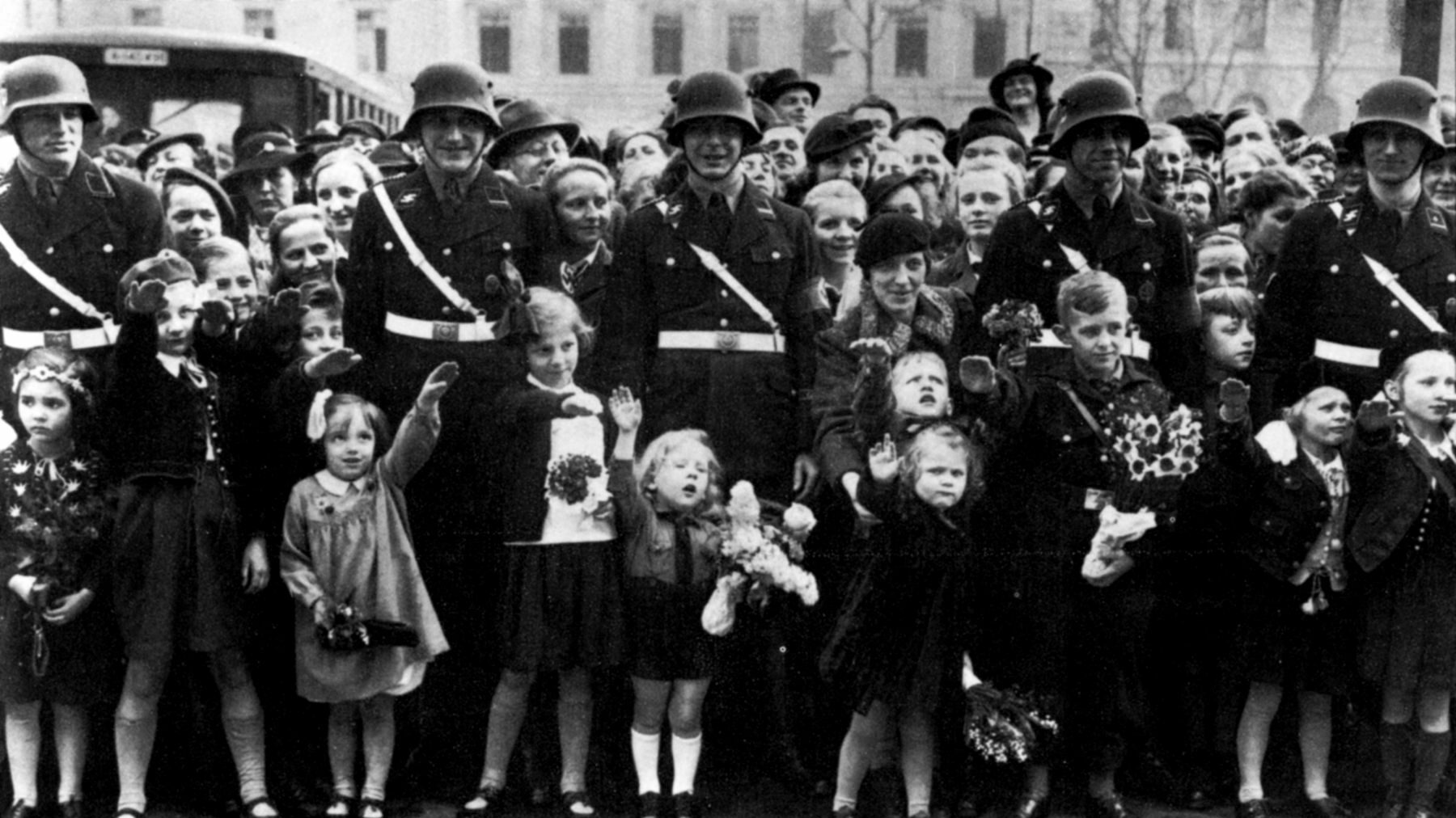 A throng of mesmerized children attempts to squeeze between smiling SS guards to deliver the Nazi salute during a party rally. Children were intensely indoctrinated in the Third Reich and made to practice the salute along with a “Heil Hitler!” to increase their devotion to the regime.