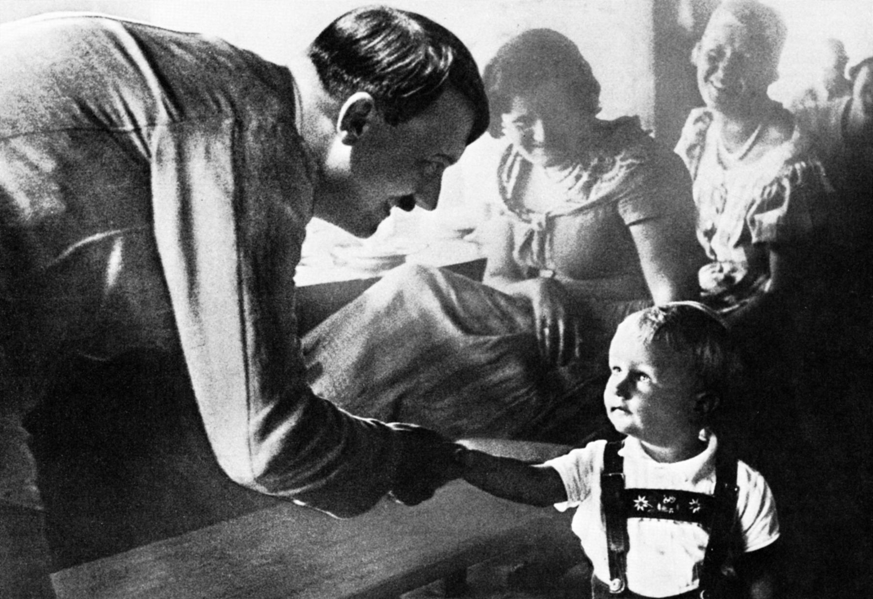 Hitler stoops to greet a wide-eyed German boy wearing native lederhosen in this propaganda photo, which was widely distributed in Germany and abroad.  Note the approving adults seated in the background.