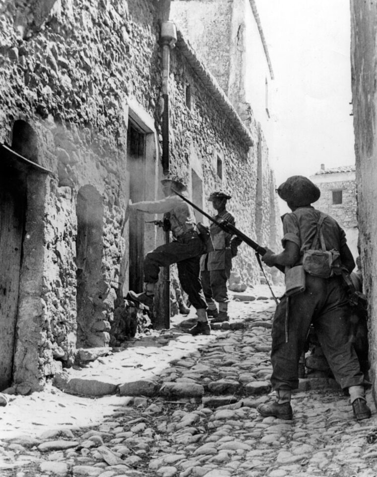 Searching for enemy snipers, a group of British infantrymen prepare to break down a door in the Sicilian town of Centuripe. 