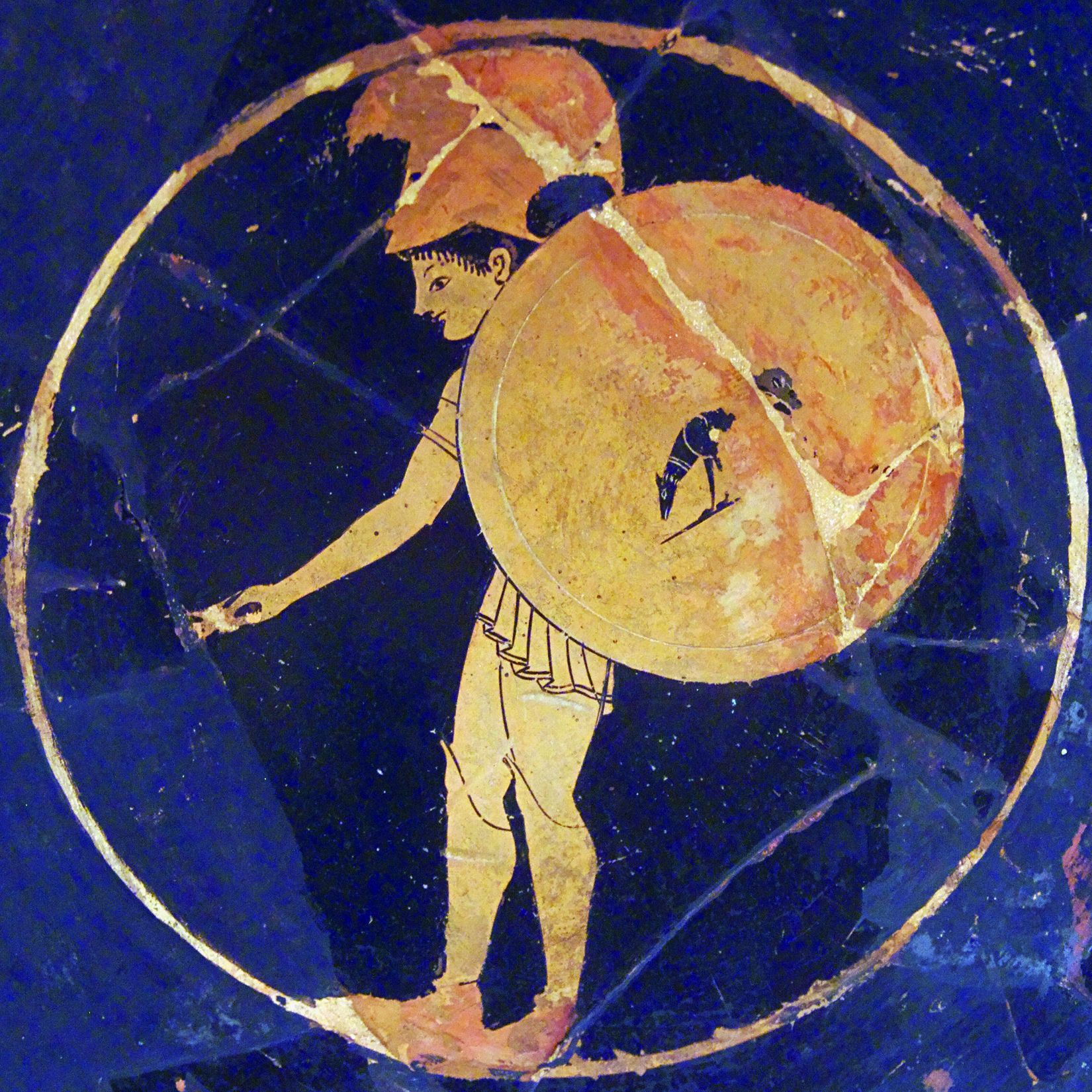 A savage hoplite flourishes a shield decorated improbably with the drawing of a dog.