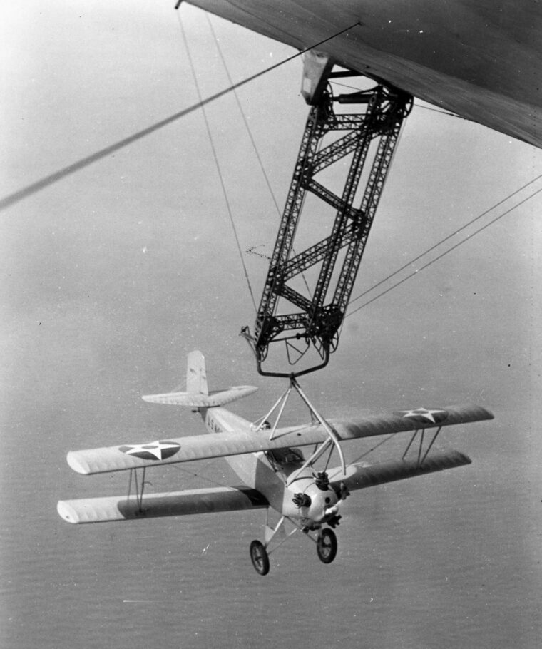 In flight, a biplane tests the hook-on device attached to the bottom of the USS Akron.