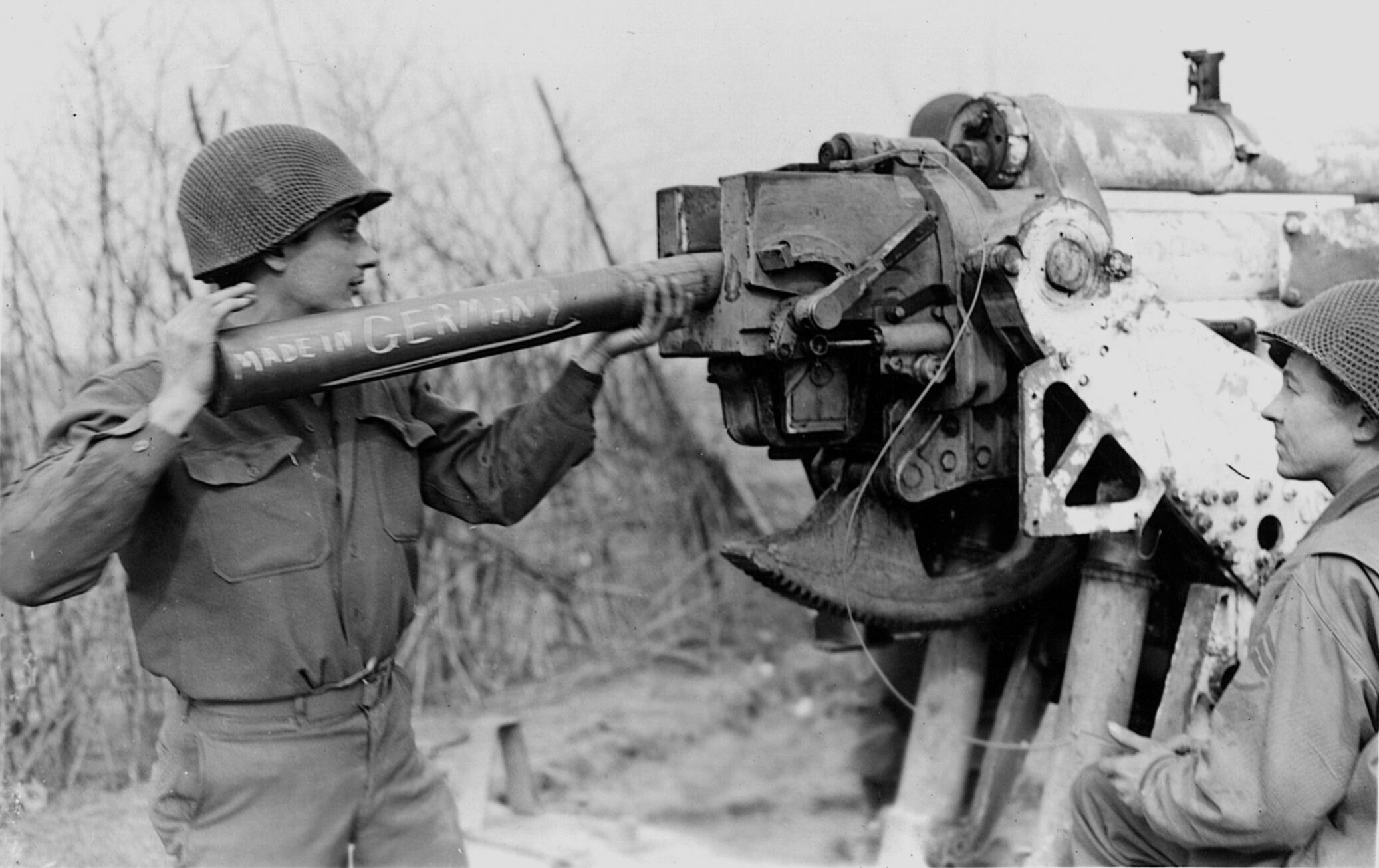 Turning the enemy’s own 88mm gun on them, a soldier loads the notorious weapon with a shell inscribed “Made in Germany” and prepares to fire across the Rhine River.