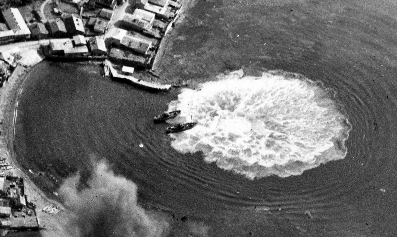 In the wake of a strike by carrier-based aircraft of the U.S. Third Fleet on July 26, 1945, port facilities on the northern coast of the Japanese Home Island of Honshu burn fiercely. 
