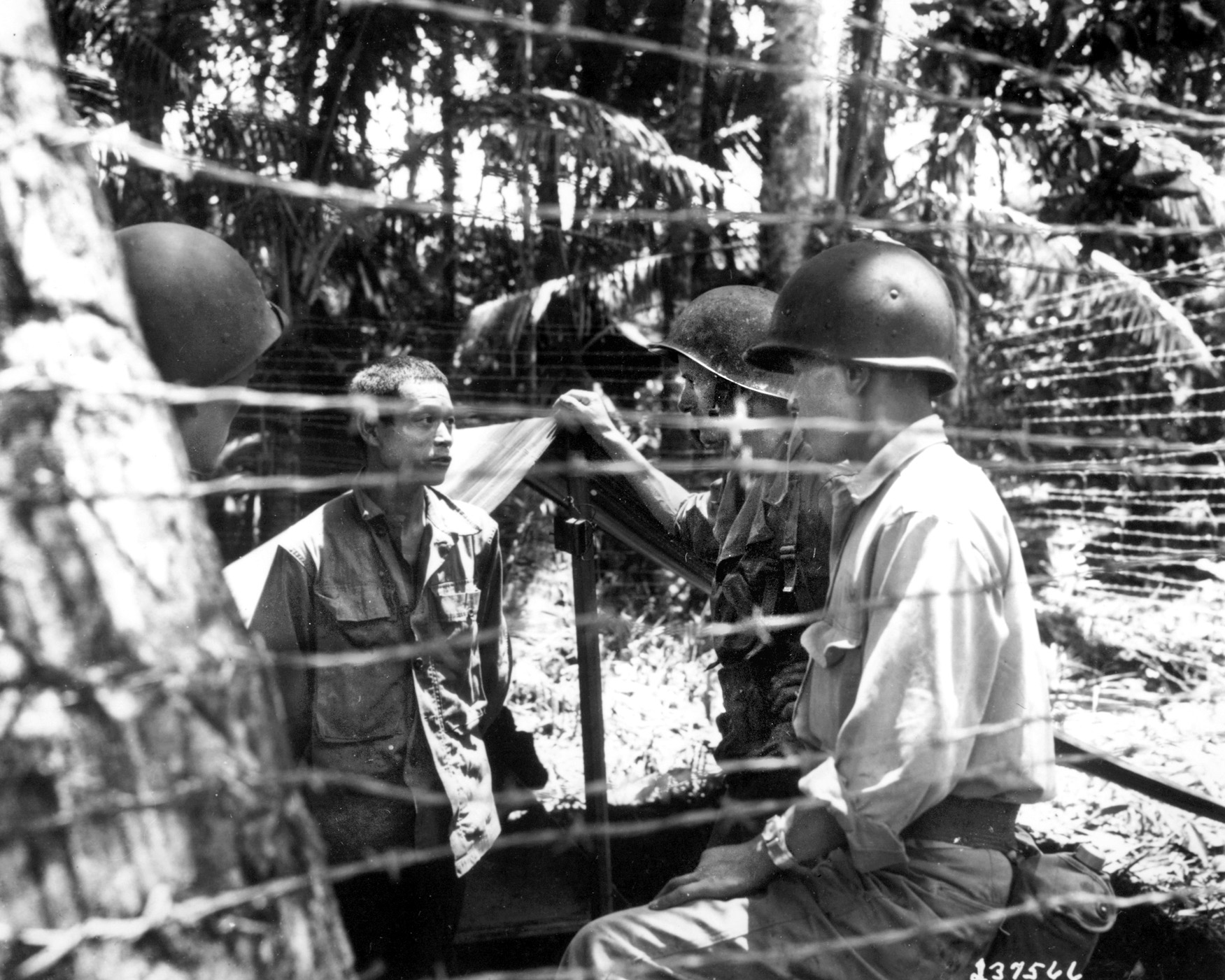 On September 12, 1943, at Vella Lave, New Caledonia, Major John Burden and Nisei soldiers of the 25th Division Language Section, attached to G2 (Military Intelligence), interrogate a Japanese prisoner of war in a temporary stockade.