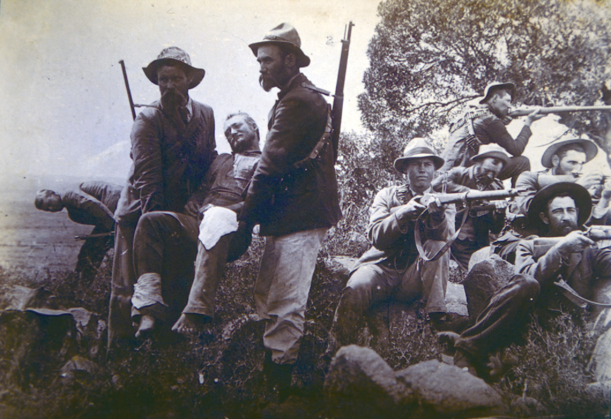 A badly wounded Boer is carried out of danger as his comrades keep watch with their Mausers. 