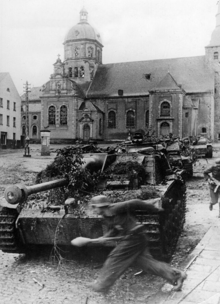 German tanks and panzergrenadiers assemble in the town square of Aachen prior to mounting a counterattack against advancing American troops. A Volkssturm panzergrenadier is seen sprinting past a Sturmgeschutze assault gun with a Panzerfaust antitank weapon in hand. (Both: National Archives)