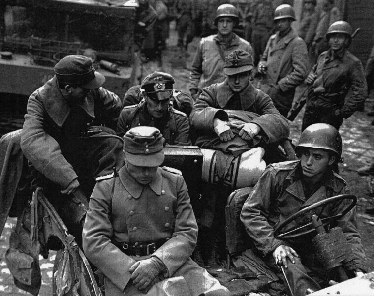 German officers, surrounded by their American captors, appear despondent after the fall of Aachen. Following weeks of severe fighting, the first major city in Germany had been taken by Allied troops. 