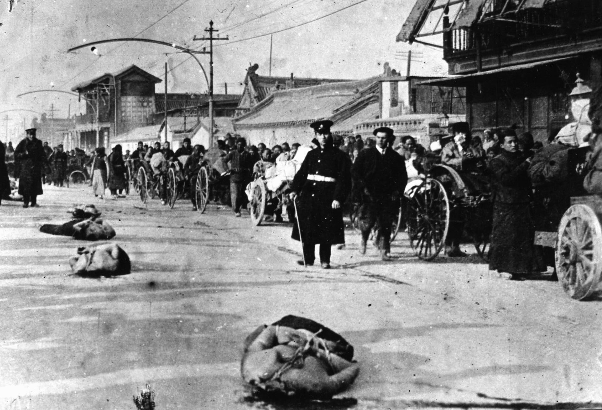 Left lying where they fell, Chinese victims of a Japanese execution lie bound and lifeless on a city street. The line of Chinese refugees fleeing the fighting seems hardly to take notice. (National Archives)