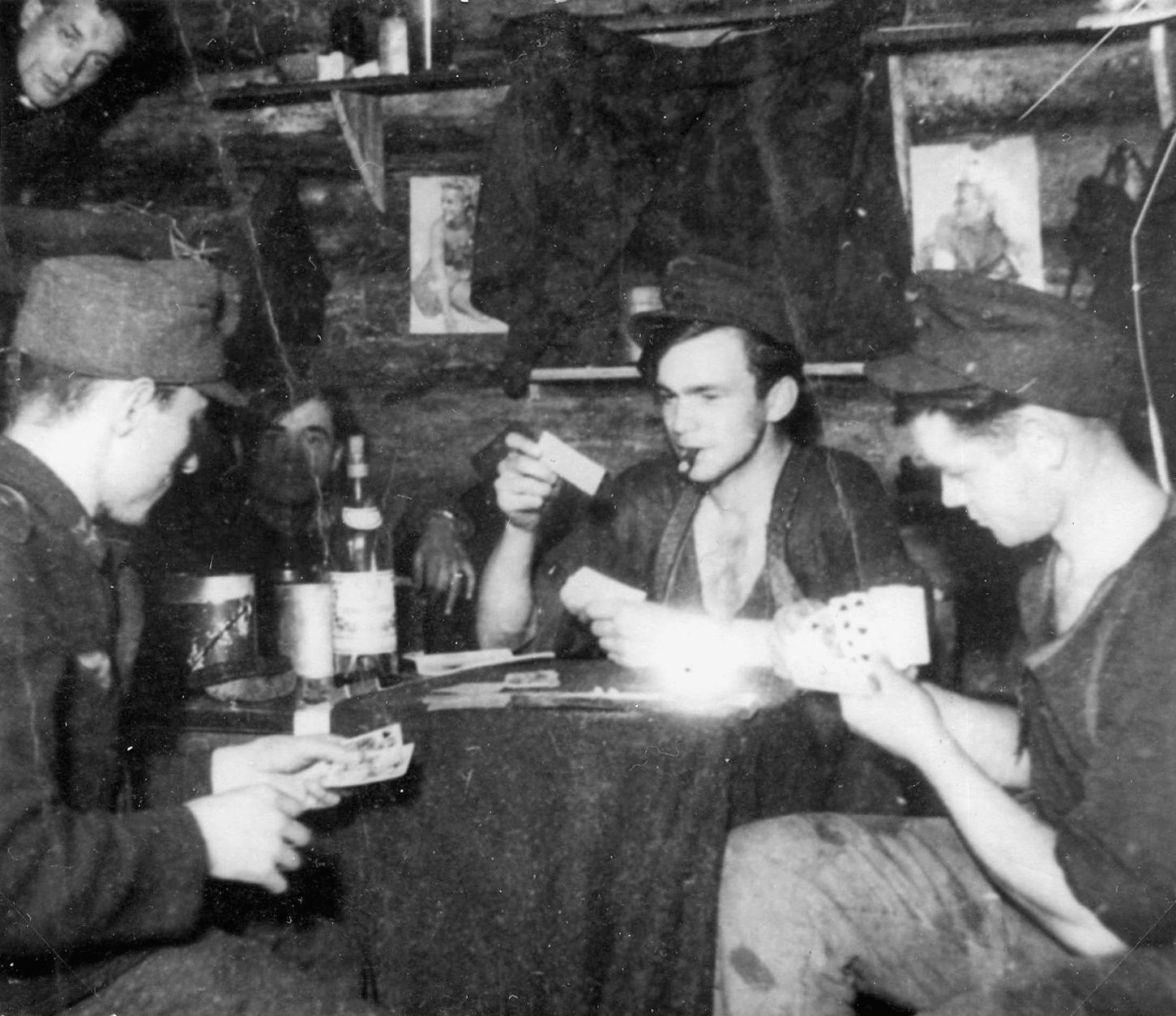 Playing a favorite card game called Skat, several soldiers find a moment of relaxation. Louis Petersen, a cigar hanging from his mouth, raises a card to trump one of his opponents.