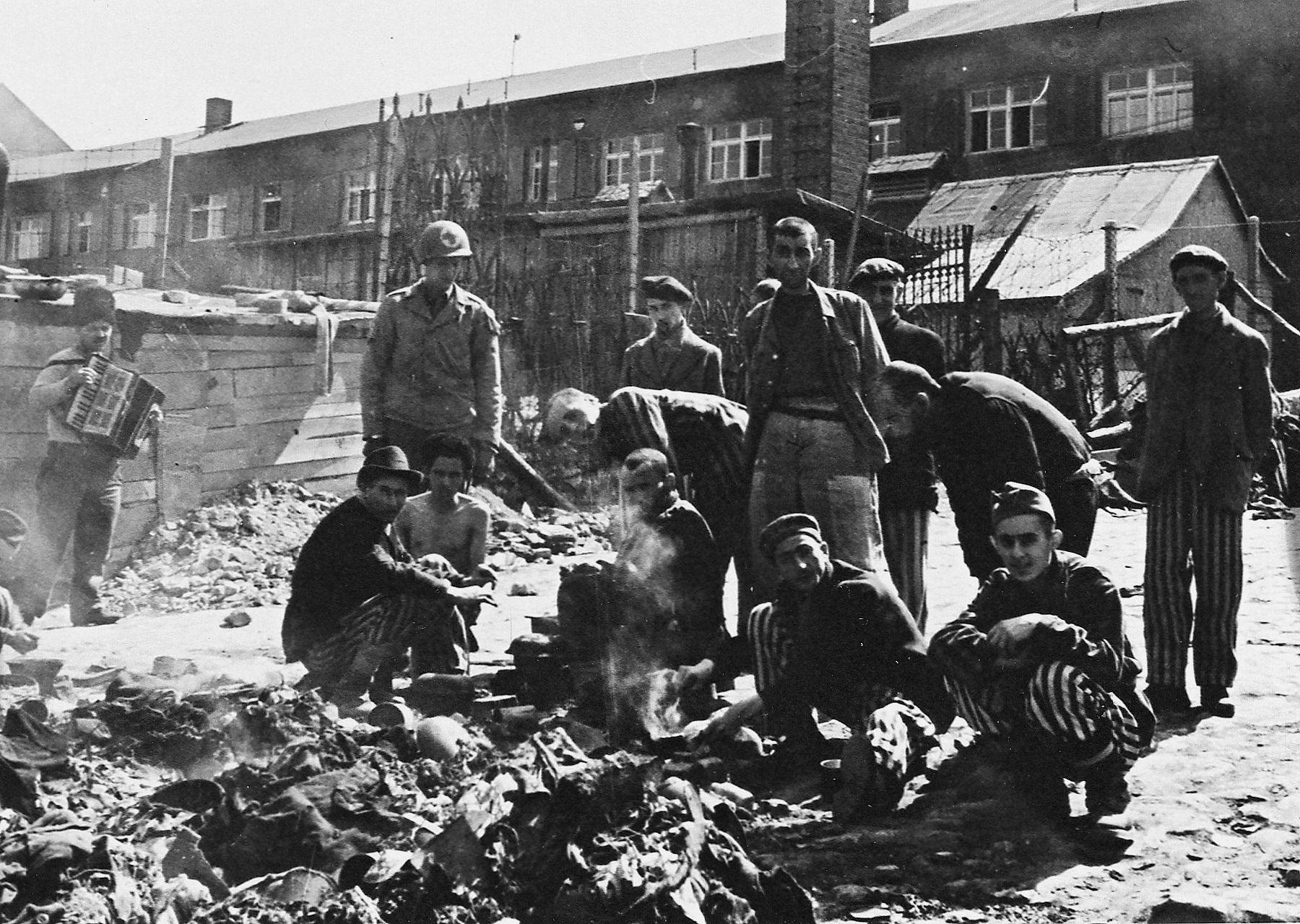 A large group of Buchenwald inmates huddles around an open cooking fire while an American soldier observes. Some inmates had been starved for such prolonged periods that their overconsumption of food following liberation became fatal. (National Archives)