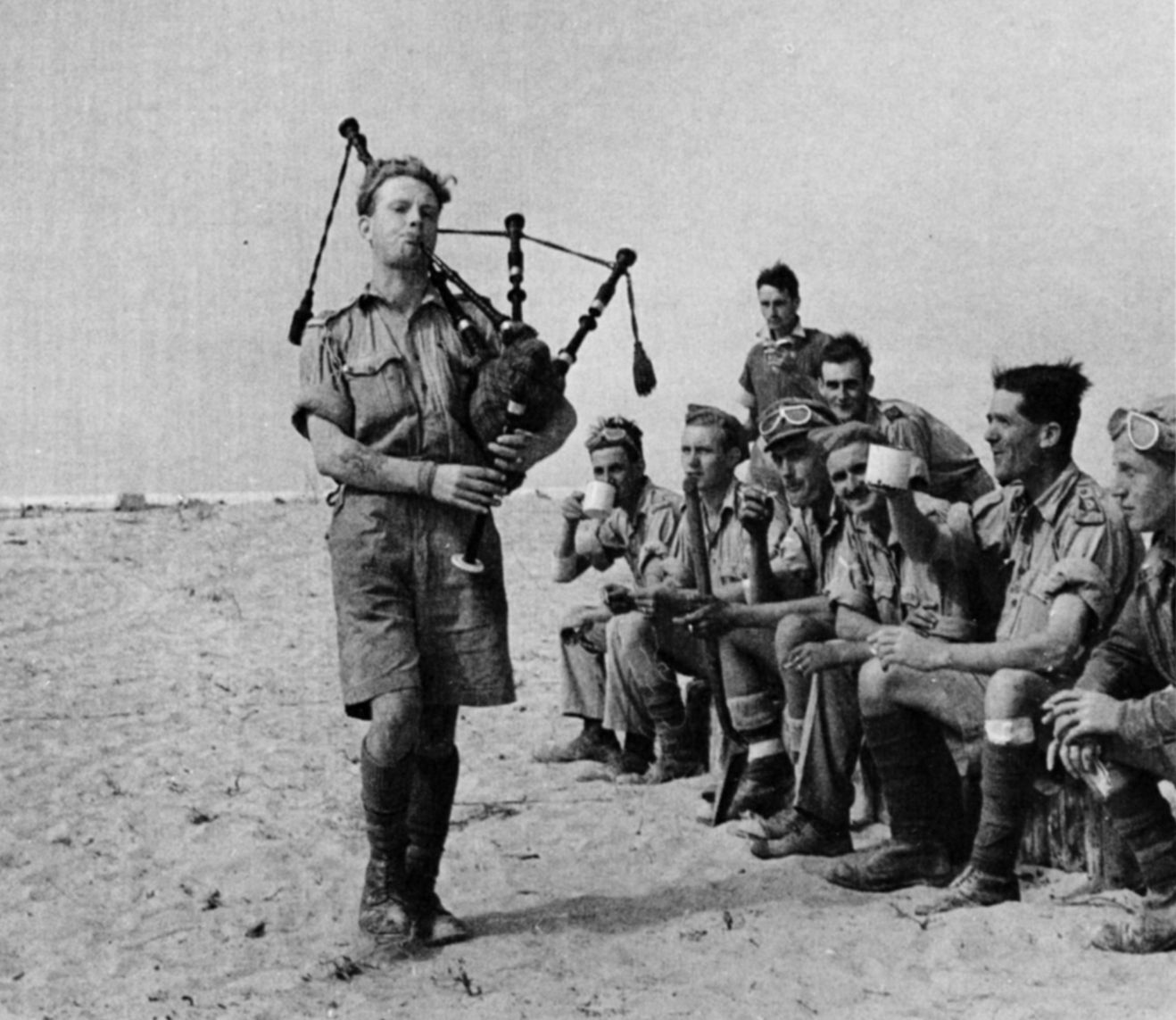 During a lull in the desert fighting, a bagpiper entertains British soldiers with an impromptu concert.