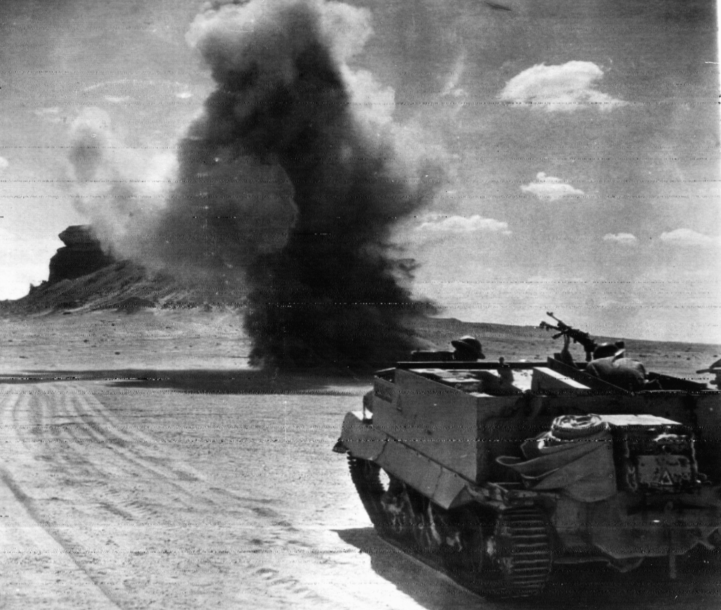Patrolling in their Bren gun carrier, a group of British soldiers comes under fire from German artillery positioned beyond the desert horizon.