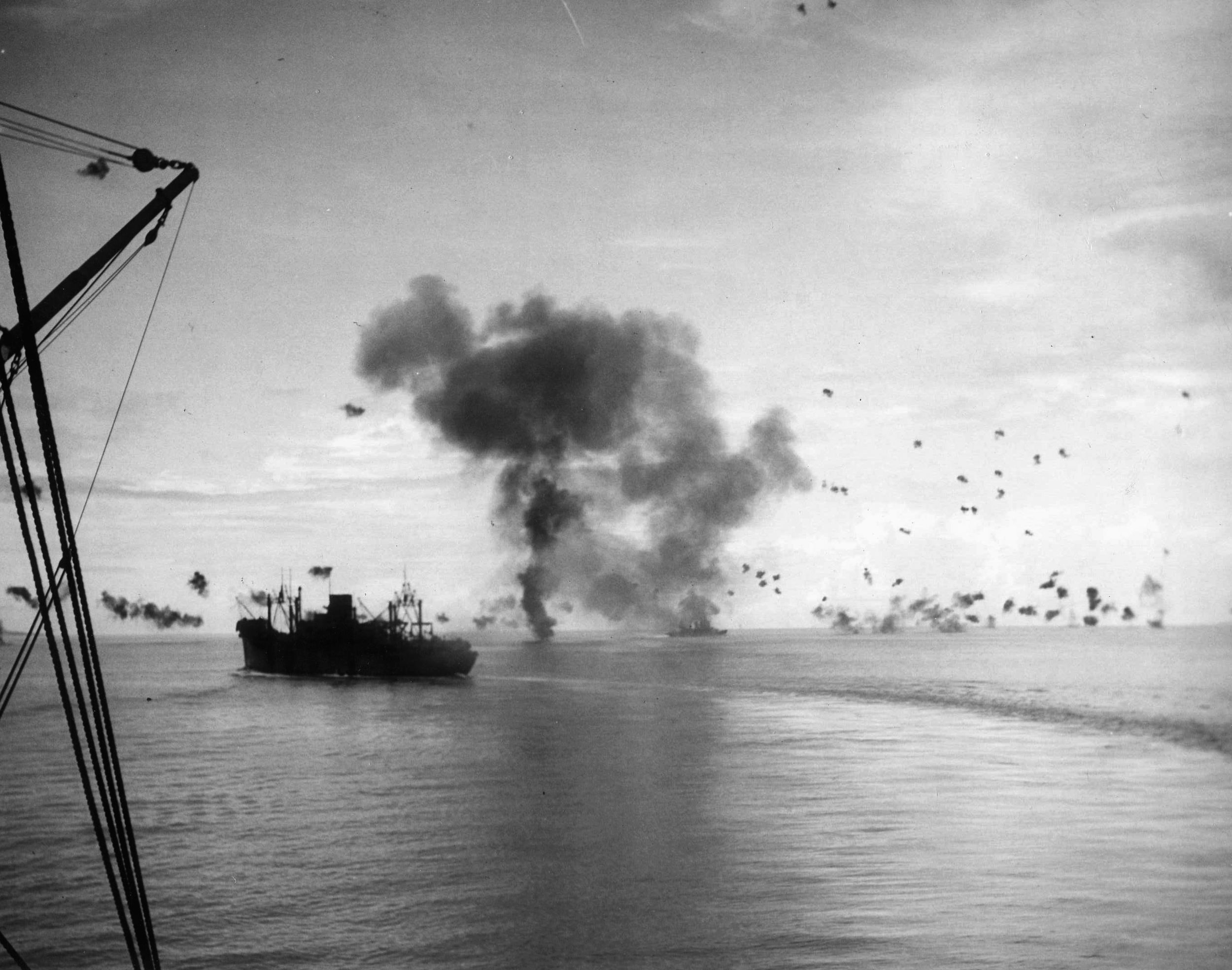 The transport vessel USS President Jackson turns hard to port in the vicinity of the Solomons, while smoke rises from the cruiser USS San Francisco after a Japanese plane has crashed into its superstructure. 