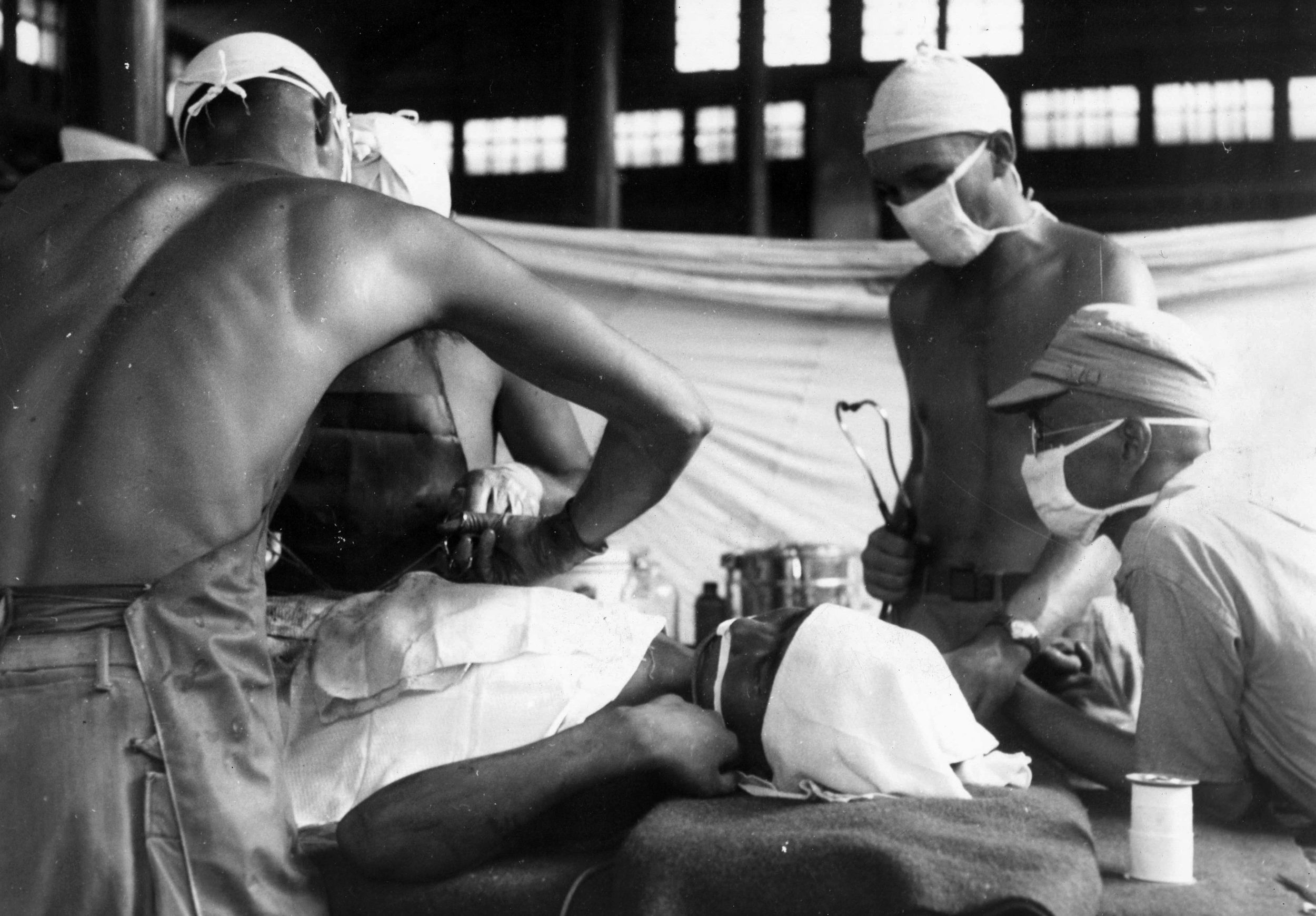 An American surgeon and his attending orderlies perform surgery on a wounded Chinese soldier in the recently liberated Chinese city of Kwelin. This operation is taking place at a Portable Surgical Hospital, a facility established in close proximity to the front lines.