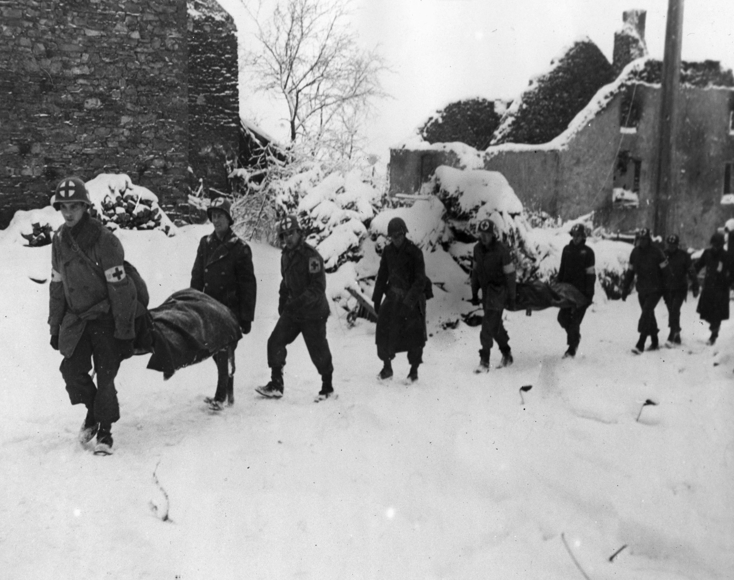 Medical personnel of the U.S. 35th Infantry Division carry litters of wounded soldiers toward the rear near the snow-covered town of Lutrebois, Belgium.