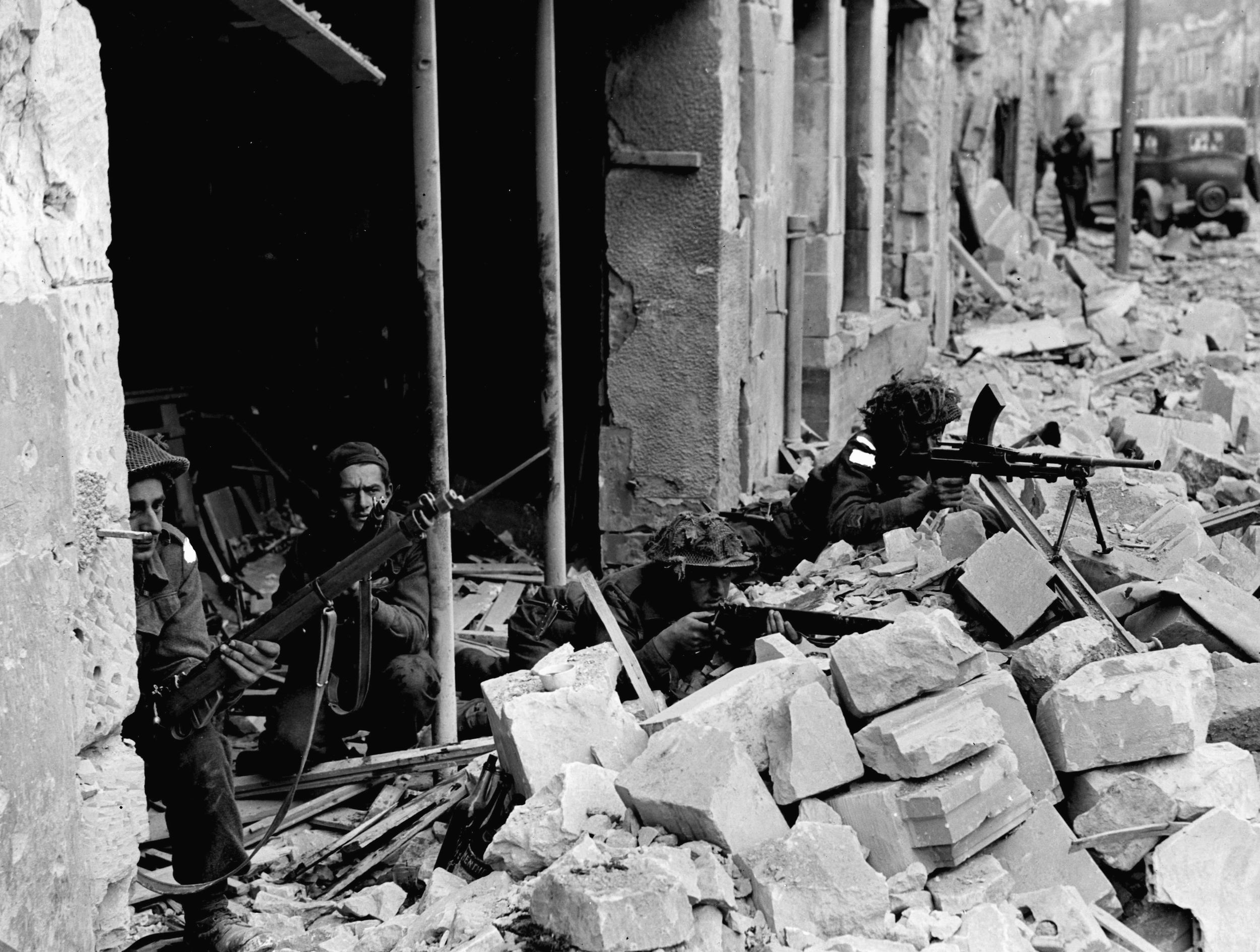 Attempting to pinpoint the locations of German snipers hiding on the upper floors of nearby buildings, Canadian soldiers take cover amid the ruins of the embattled town of Caen. The initial plan for Operation Overlord called for the capture of Caen on D-Day. However, the city remained in German hands for another month. 
