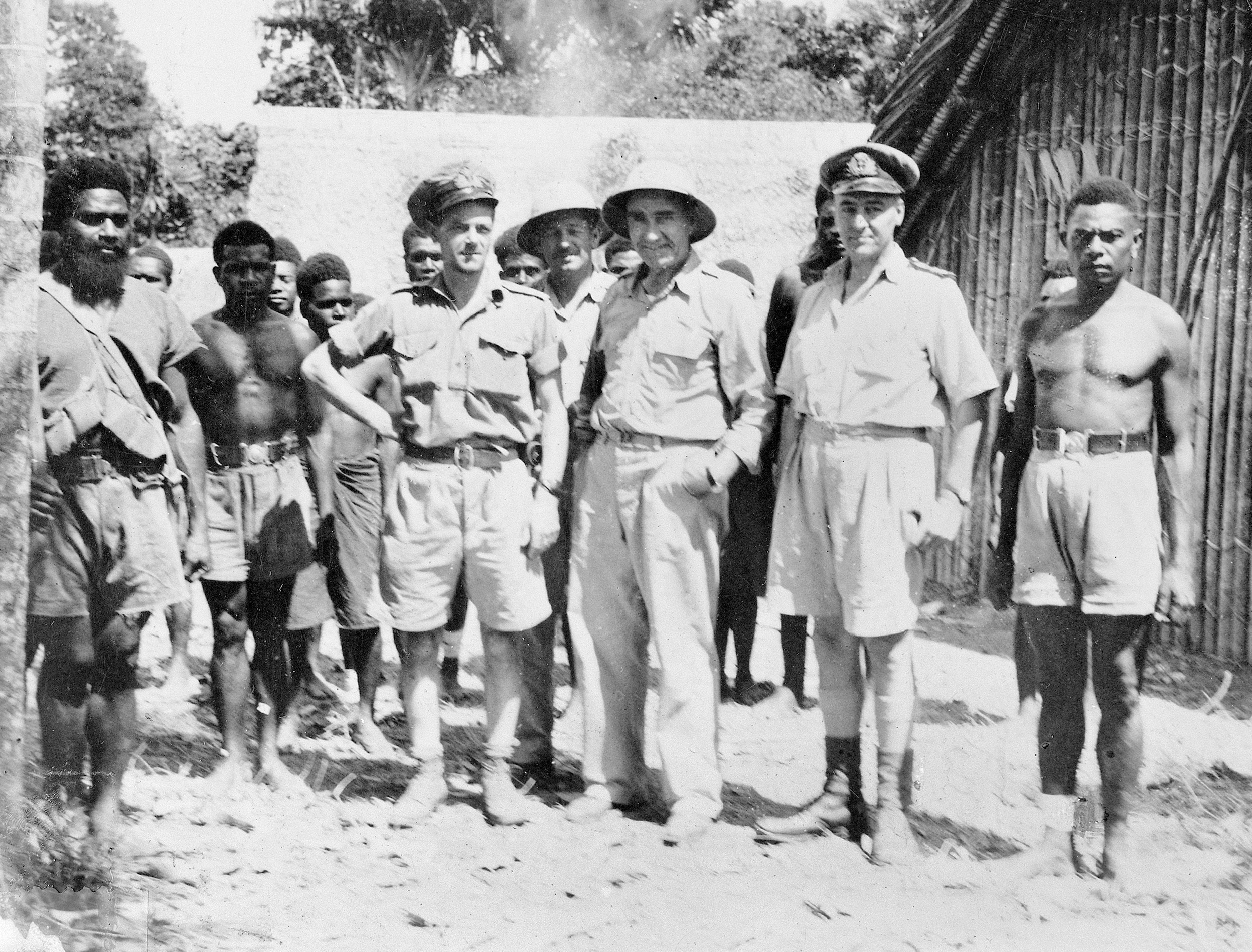 Lt. Cmdr. W.J. “Jack” Read of the Royal Australian Navy Intelligence Division poses (hand on hip) with other personnel, including native scouts, at the Australian Intelligence Bureau Camp at Lunga, Guadalcanal, on March 27, 1945. 