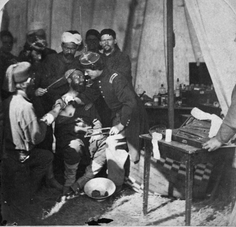 Zouave soldiers prepare an injured comrade for the amputation of his right arm while surgeons stand by with their instruments in this possibly staged photograph. 