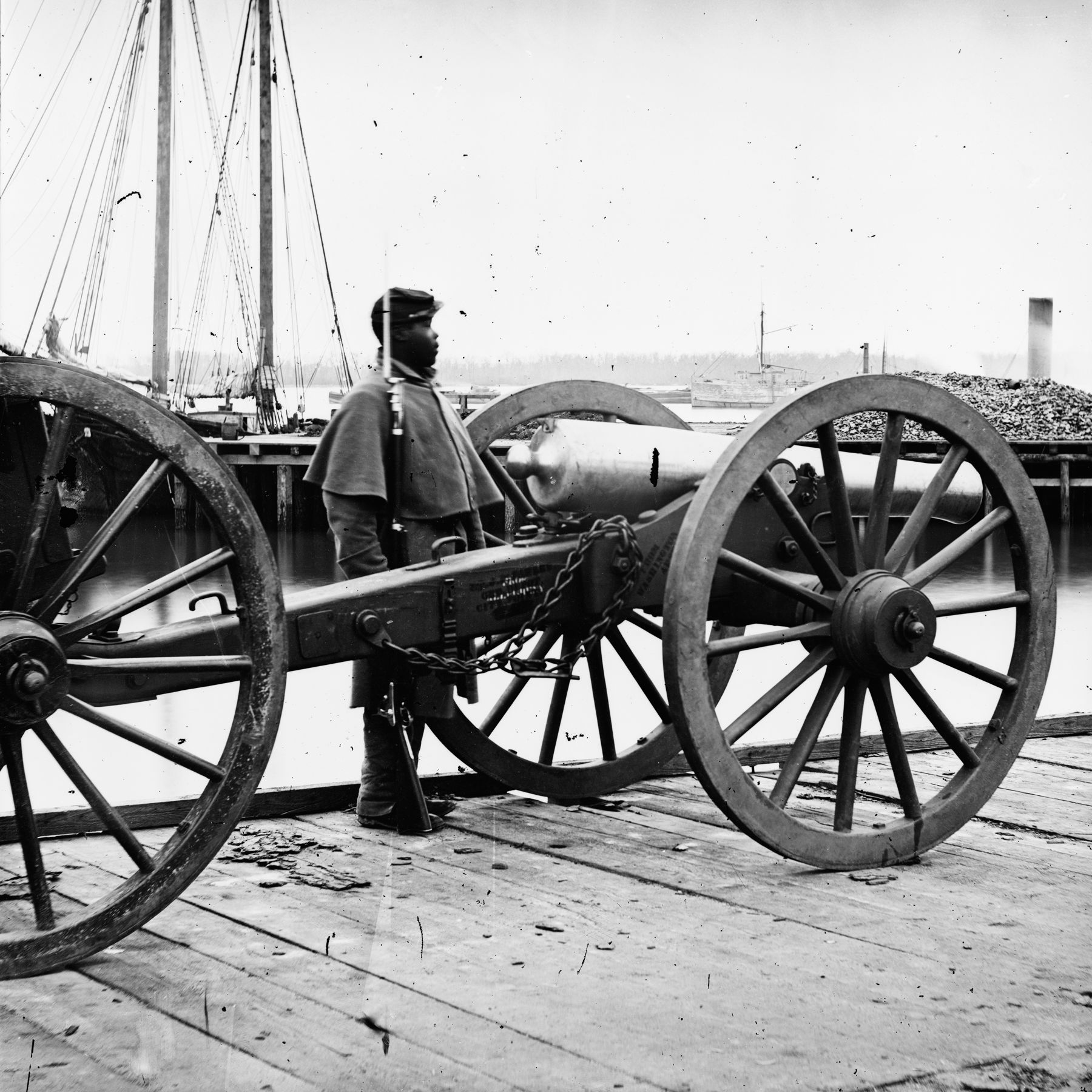 An African American soldier stands watch over a Union 12-pounder during the Civil War.