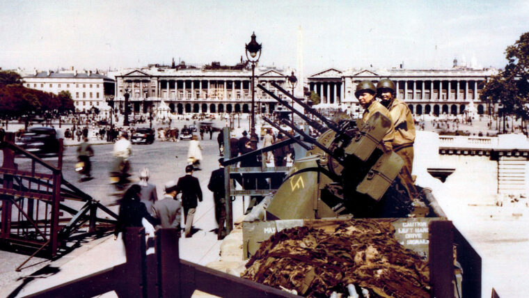 Soldiers man a quad .50 anti-aircraft gun on the Place de la Concorde. Behind them stands the Hôtel de Crillon on the left, the Obelisk of Luxor in the center, and the Church of Madeline, to the immediate right of the Obelisk, and the French Naval Ministry on the far right. Belgian gates—German anti-tank obstacles—surround the gun nest.