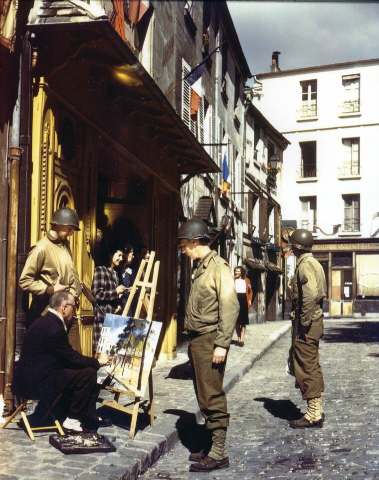 Two American soldiers watch a street painter complete his canvas, while a third enjoys a different view.