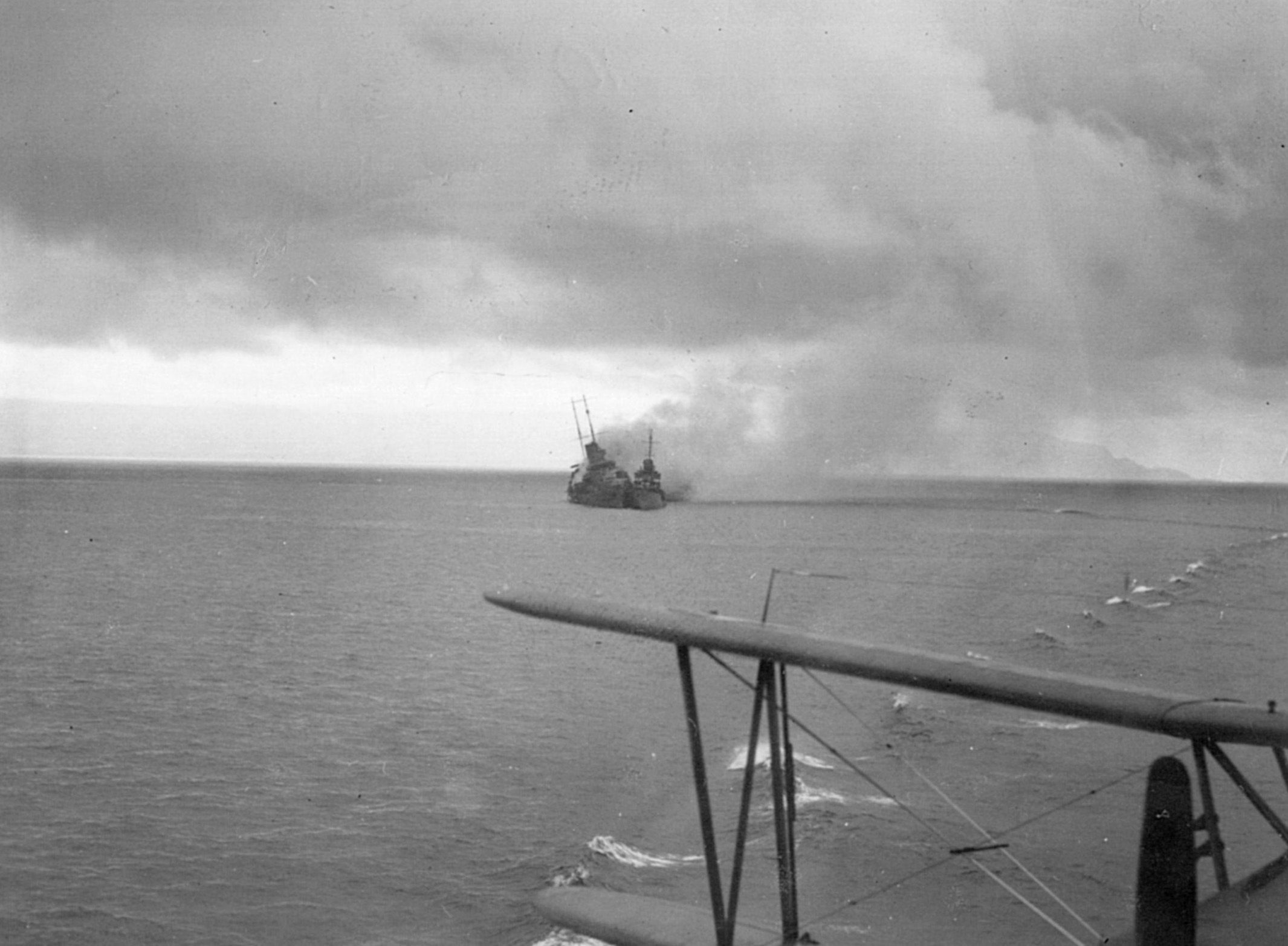 In a photograph taken from the deck of the USS Chicago, the Australian cruiser Canberra lists to starboard and belches smoke as a destroyer pulls alongside to rescue crewmen.