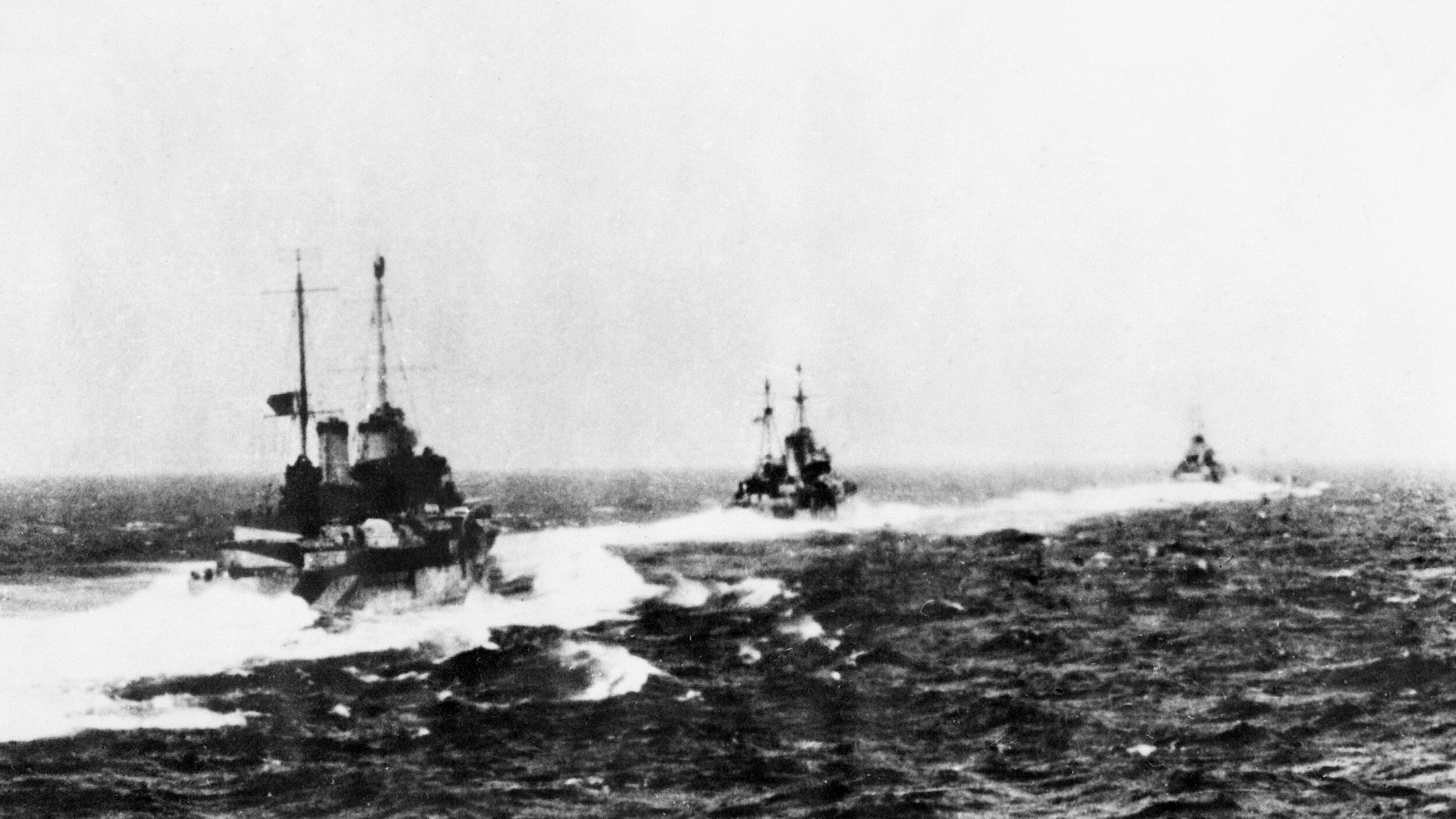 Seen from the deck of the Royal Navy cruiser HMS Gloucester, the British cruisers Ajax and Orion sail in company with the Australian cruiser HMAS Perth.