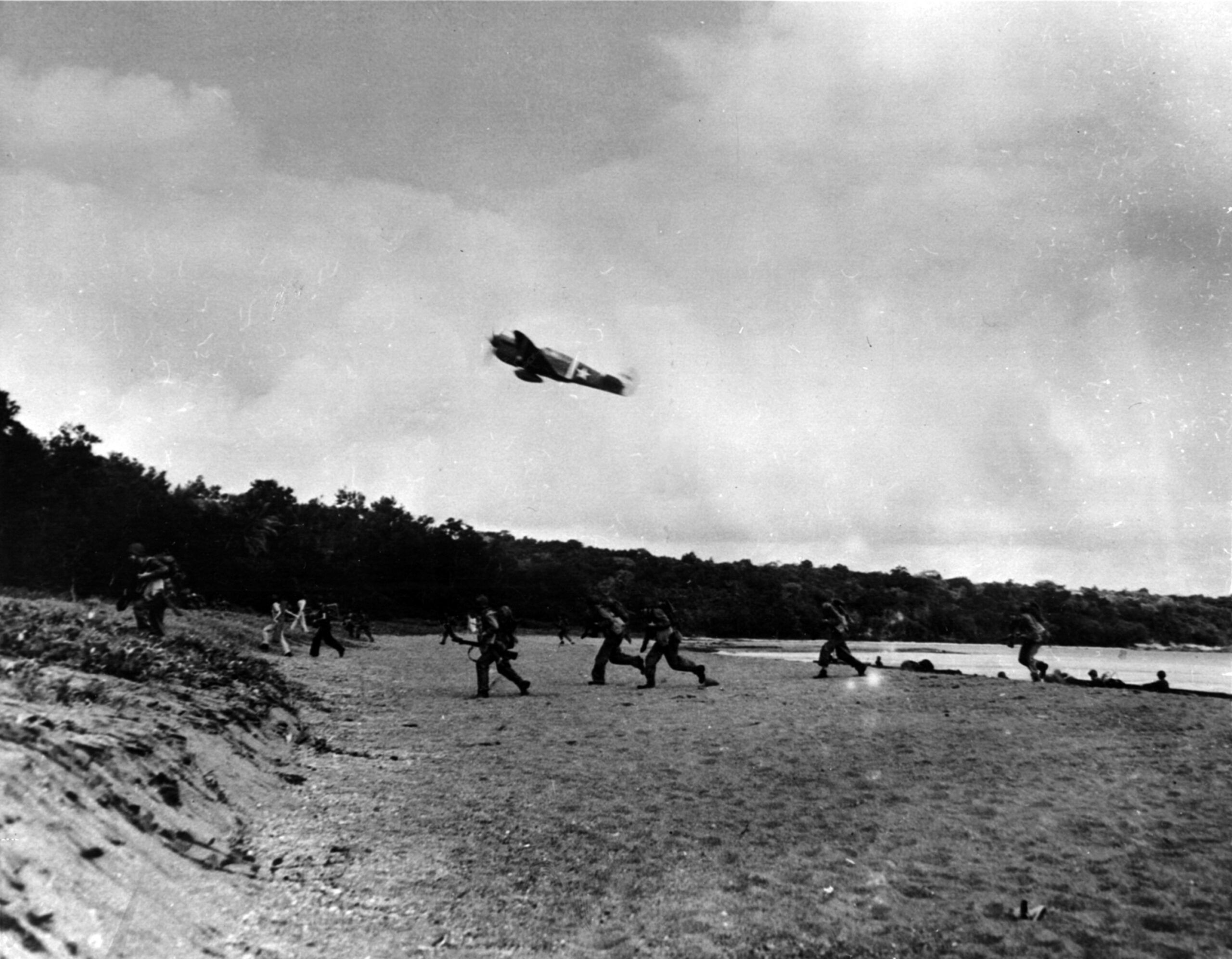 Providing aircover for troops landing at Rendova, a P-40 Tomahawk fighter sweeps low over the invasion beach. 