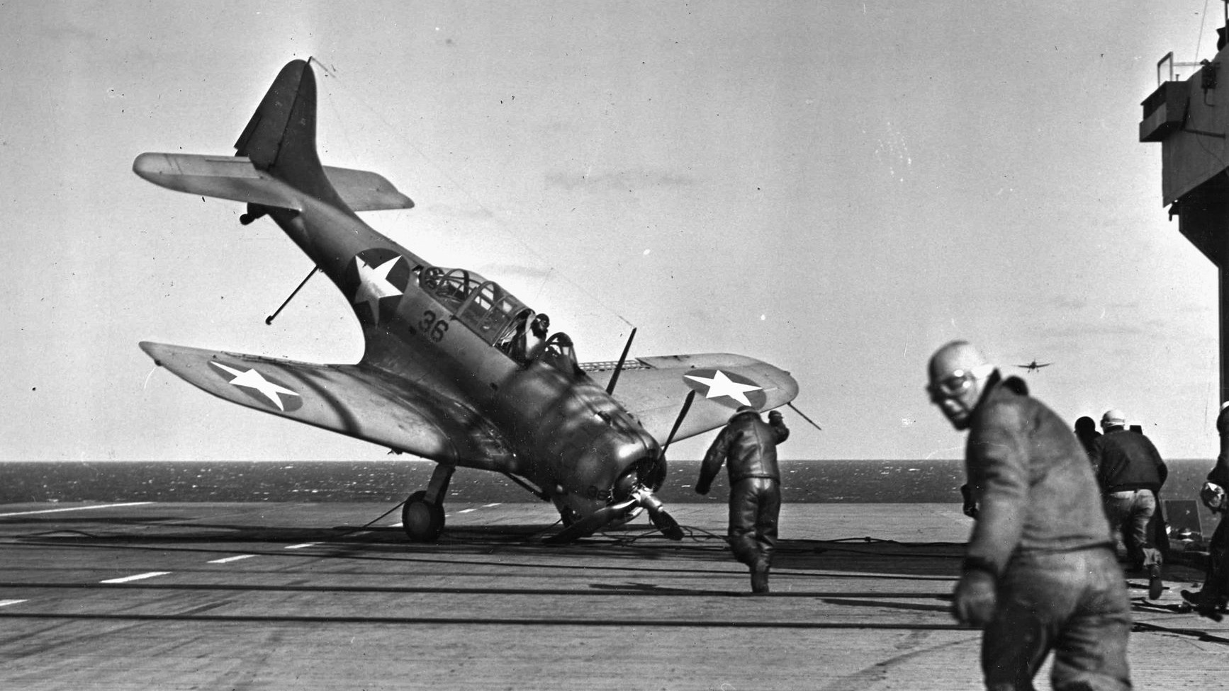 Deck crewmen race to an SBD Dauntless dive bomber after a barrier crash. The extended tailhook failed to catch the arresting wire, but the propeller stopped the forward momentum, almost flipping the plane. Aviators claimed that SBD stood for “Slow But Deadly.”