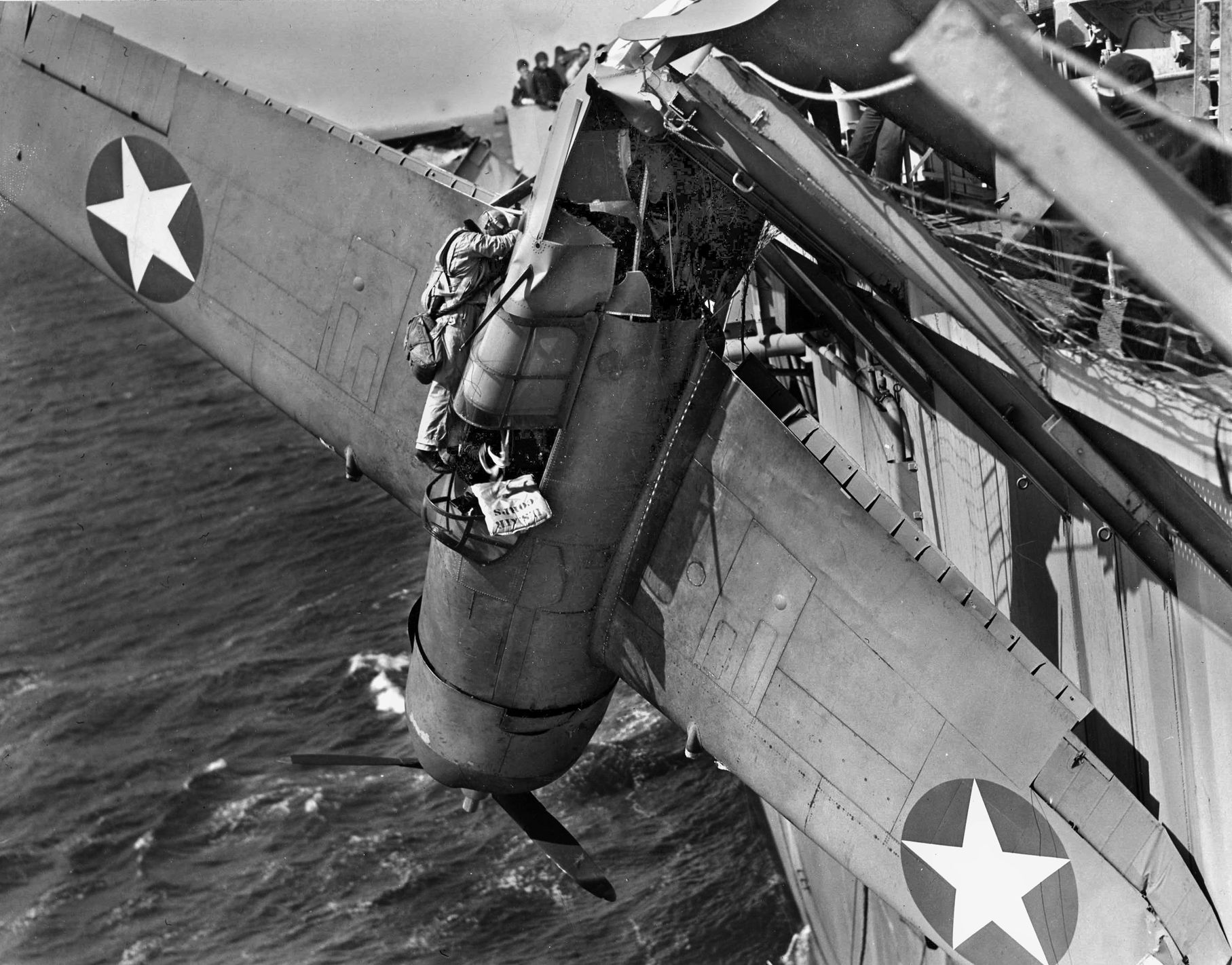 A student aviator gingerly climbs out of his dangling F4F Wildcat. A rope around his waist prevents  him from falling into  the icy brine of the North Atlantic.