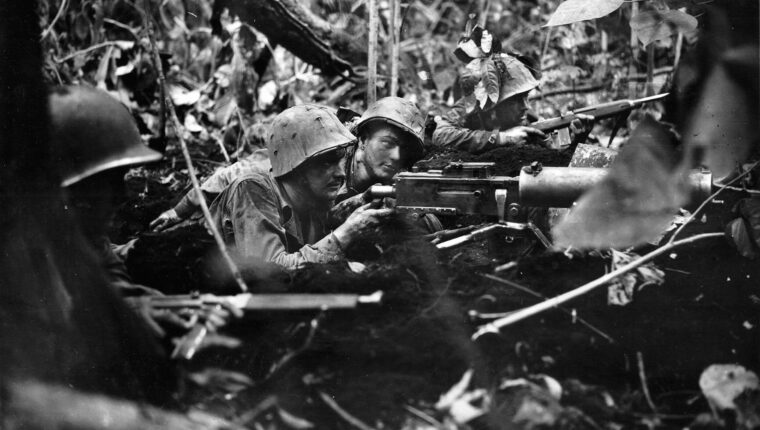 Using a machine gun and carbine rifles, infantrymen sight up enemy positions during an attack on Cape Gloucester.