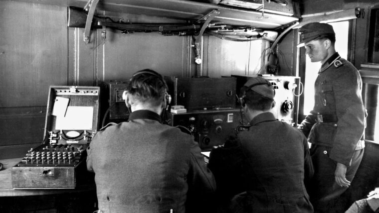 German soldiers operate an Enigma machine, sending classified information encoded through a system of rotor settings that were believed to be virtually impossible to crack. However, Allied cryptanalysts at Bletchley Park were reading top secret German communications for some time during World War II.