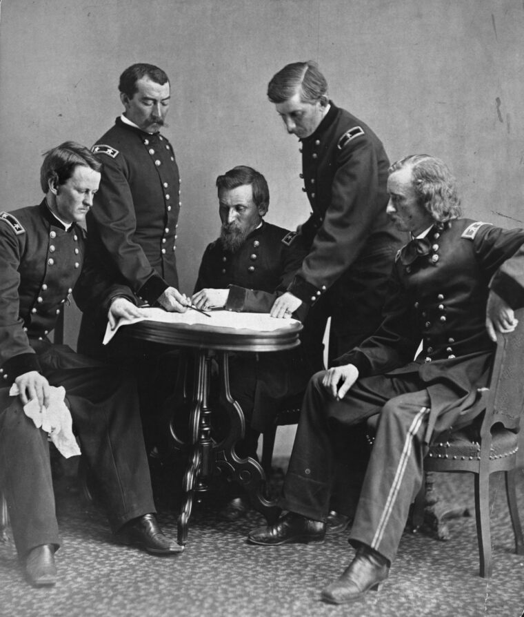 Sheridan, standing left, goes over a battle map with his staff, including, left to right, Wesley Merritt, George Crook, William Forsyth, and George Armstrong Custer.