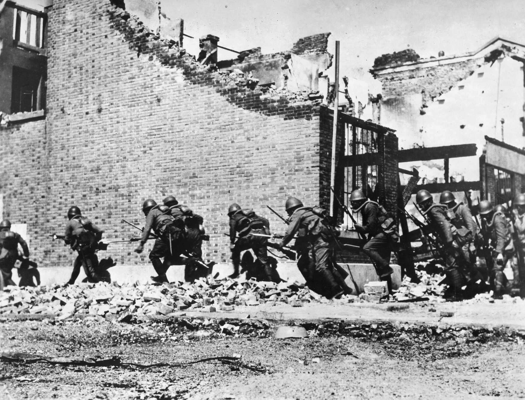 Flourishing bayonets, a Japanese landing unit hugs a shattered wall as it advances on a Chinese position in Zhabei.