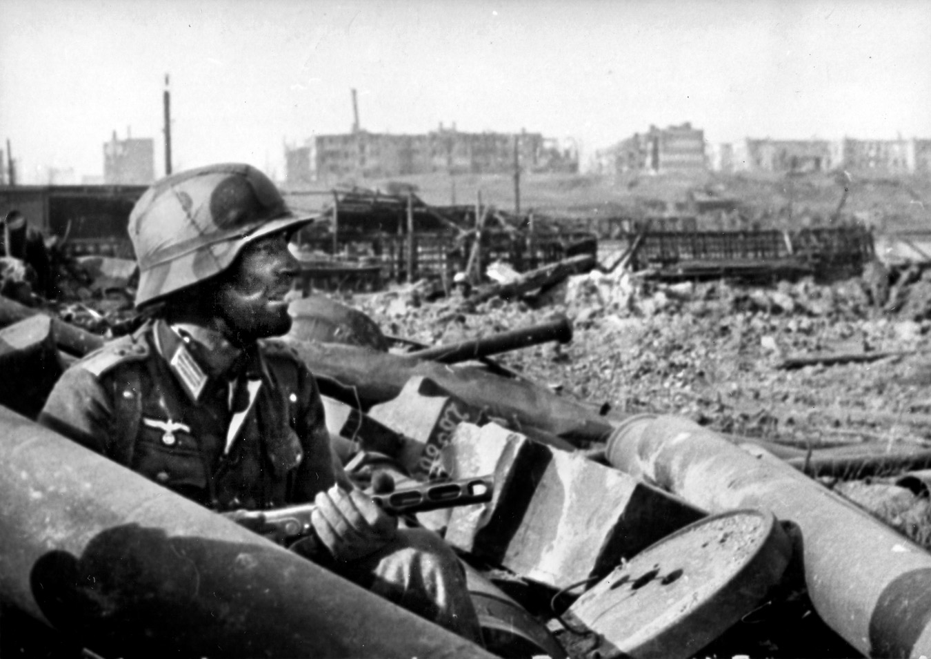 A battle-weary German lieutenant armed with a captured Soviet PPSh41 sub-machine gun peers cautiously out of the rubble at Stalingrad. 