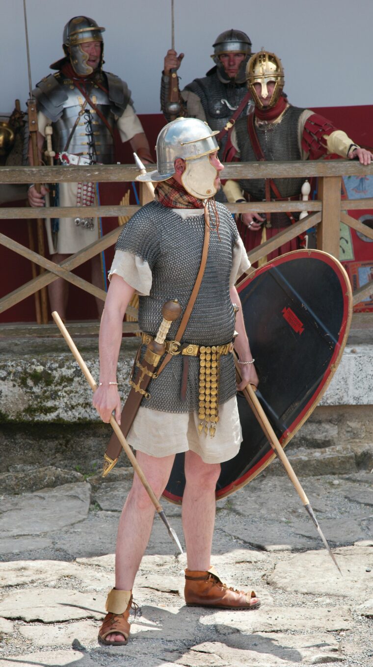 A Roman reenactor wearing chain mail, armed with a gladius sword and pilum javelins.